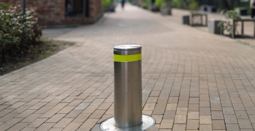 Stainless steel security bollard installed on a pedestrian pathway, demonstrating access control and safety in a commercial setting.